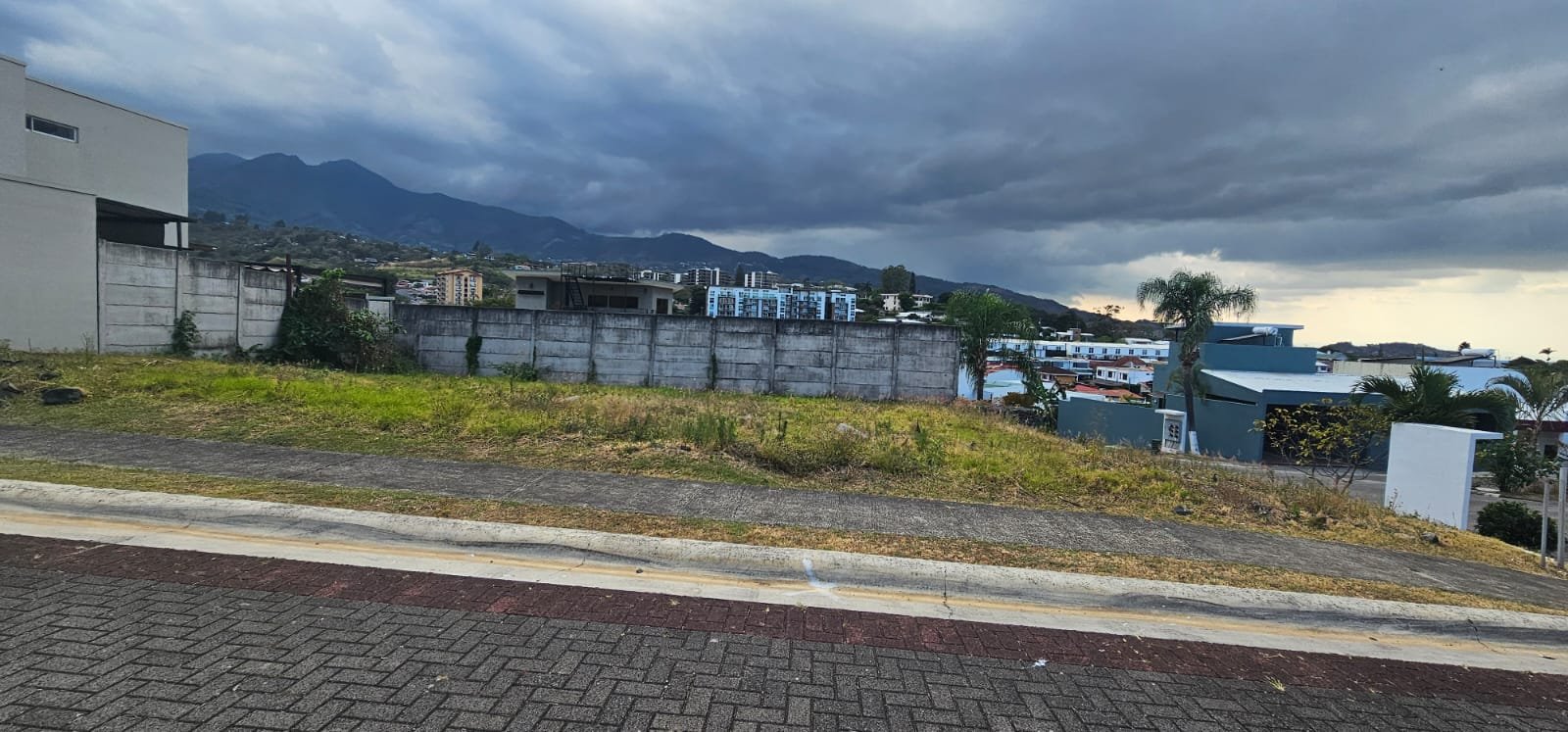 Vista a nivel de calle del lote esquinero en Rivergrand con montañas de Escazú